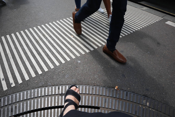 часть тела, пара граждан в костюмах, переходящих дорогу на пешеходном переходе и женская нога на крышке люка, пересечение зебры - Фото, изображение