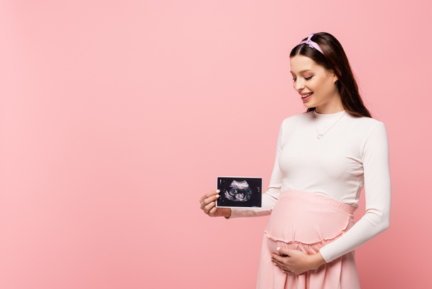 happy young pretty pregnant woman holding ultrasound scan isolated on pink - Foto, afbeelding