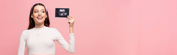Ευτυχισμένη νεαρή όμορφη έγκυος γυναίκα κρατώντας υπέρηχο σάρωση απομονωμένη σε ροζ, πανό - Φωτογραφία, εικόνα