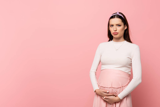 sad young pretty pregnant woman touching belly isolated on pink - Foto, afbeelding