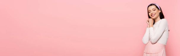 happy young pretty pregnant woman with closed eyes isolated on pink, banner - Foto, imagen