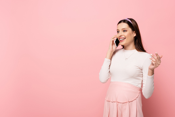 happy young pretty pregnant woman talking on smartphone isolated on pink - 写真・画像