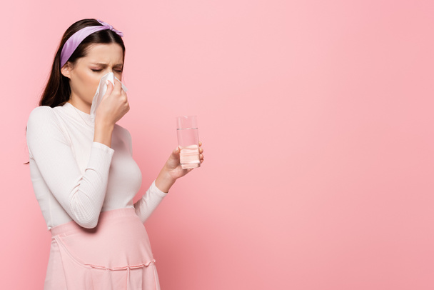 mladá hezká těhotná žena s tekoucí nos a voda izolované na růžové - Fotografie, Obrázek