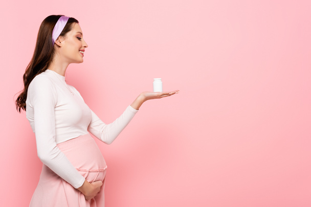 ピンク色に隔離されたビタミンを持つ幸せな若いかなり妊娠中の女性 - 写真・画像