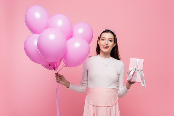 happy young pretty pregnant woman with balloons and gift isolated on pink - Foto, Bild
