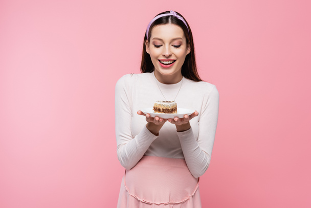 happy young pretty pregnant woman with cake isolated on pink - Foto, afbeelding
