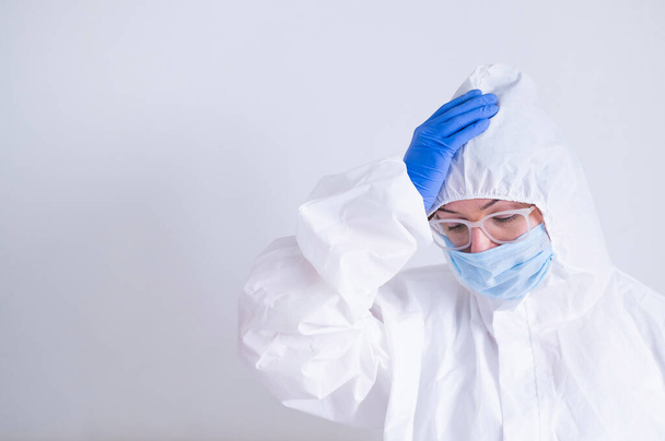 Uma mulher de fato de protecção e uma máscara médica está a segurar a cabeça. Médico virologista com problemas no trabalho - Foto, Imagem