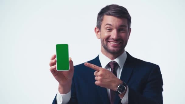 homme d'affaires joyeux pointant vers smartphone avec écran vert isolé sur blanc - Séquence, vidéo