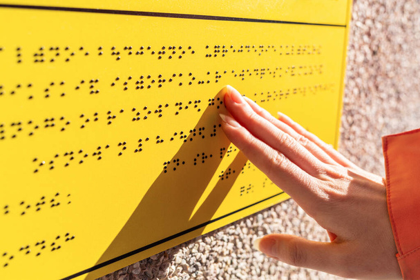 Τύφλωση. Μια γυναίκα διαβάζει μια κίτρινη πινακίδα Μπράιγ. Κλείσε τα χέρια σου. Έννοια της ημέρας των τυφλών και της αναπηρίας. - Φωτογραφία, εικόνα
