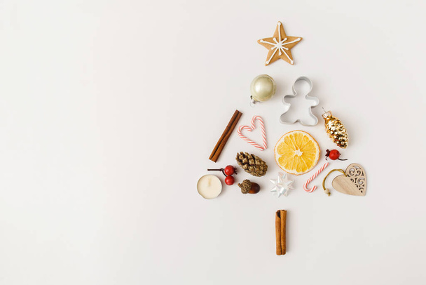 Christmas, winter, new year composition. Creative fir tree made of pine cone, cinnamon sticks, dried oranges, gingerbread on white background. Flat lay, top view, copy space - Foto, afbeelding