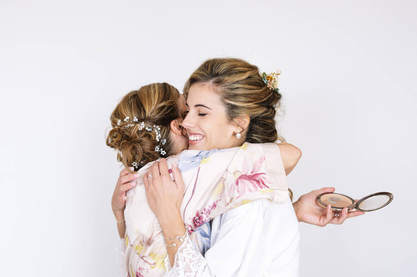 Schöne blonde Frau im weißen Kleid an ihrem Hochzeitstag vor der Hochzeit, ihre Mutter umarmt sie. - Foto, Bild