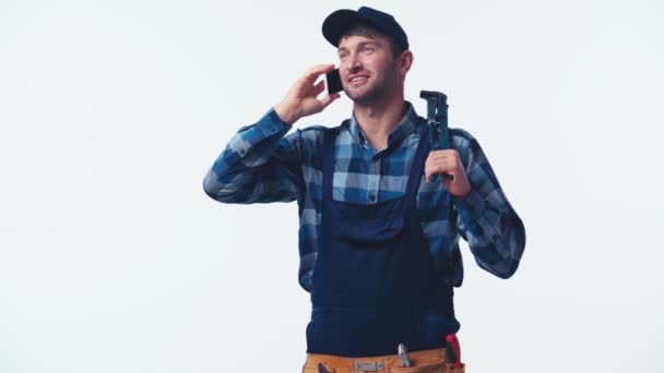 happy plumber in uniform holding pliers and talking on phone isolated on white - Footage, Video