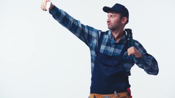 instalatér v uniformě a čepici drží kleště a přičemž selfie izolované na bílém - Záběry, video