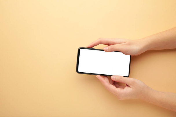 Woman hand holding the black smartphone with white screen on beige background. Top view. - Фото, зображення