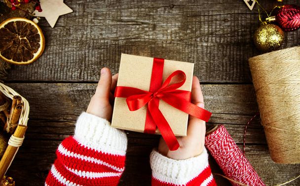 Flat lay packaging of Christmas gifts on wooden background. Children's hands are holding a gift. - Foto, Imagem