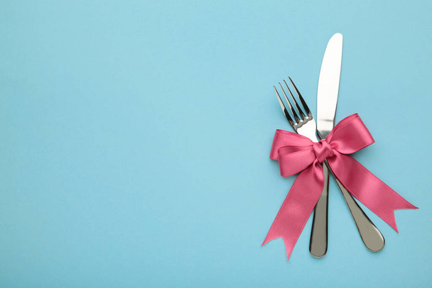 Christmas table place setting on blue background. Knife and fork with pink ribbon. Top view - Foto, Imagen