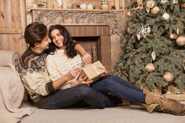 Hermosa morena caucásica pareja amorosa romántica en suéteres acogedores y cálidos en la cabaña en una víspera de Navidad de año nuevo, sonriendo, besándose, divirtiéndose entre sí. Oscuro oscuro noche luz, imagen tonificada - Foto, imagen