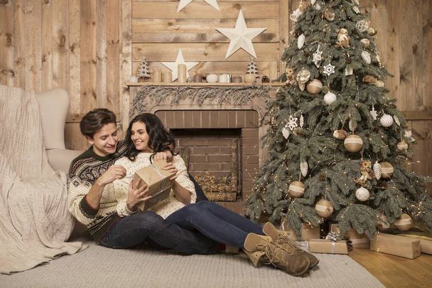 Hermosa morena caucásica pareja amorosa romántica en suéteres acogedores y cálidos en la cabaña en una víspera de Navidad de año nuevo, sonriendo, besándose, divirtiéndose entre sí. Oscuro oscuro noche luz, imagen tonificada - Foto, Imagen