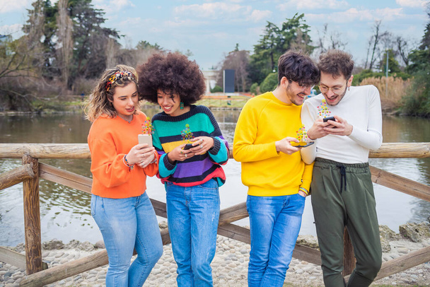 Grupo de amigos multiétnicos millennials usando teléfonos móviles adictos a las tendencias virales siguiendo y charlando usando emojis y emoticones - Foto, Imagen