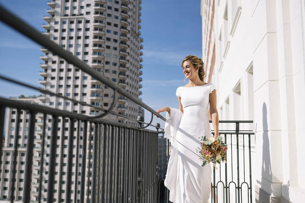 Piękna blondynka w białej sukience spacerująca po balkonie hotelu w Madrycie w Hiszpanii. W dniu ślubu przed ślubem.. - Zdjęcie, obraz