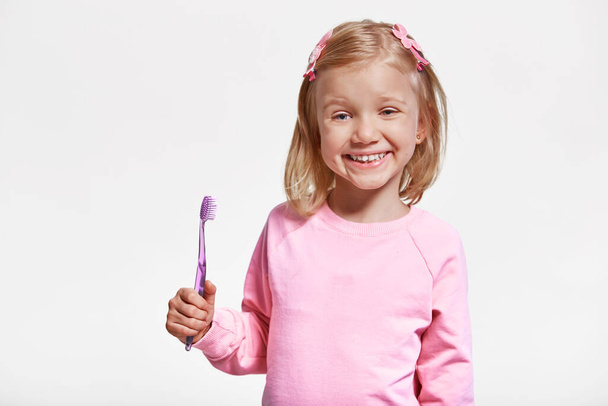 Happy child girl with toothbrush, brushes teeth and smiles on gray background. Free space for advertisement. Oral hygiene. - 写真・画像