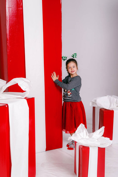 šťastný legrační dítě dívka v vánoční kostým s velkými červenými dárky na pozadí. - Fotografie, Obrázek