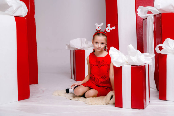 happy funny child girl in Christmas costume with big red gifts on background. - Фото, изображение
