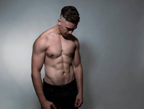 Handsome and fit bodybuilder posing on gray background  - Valokuva, kuva