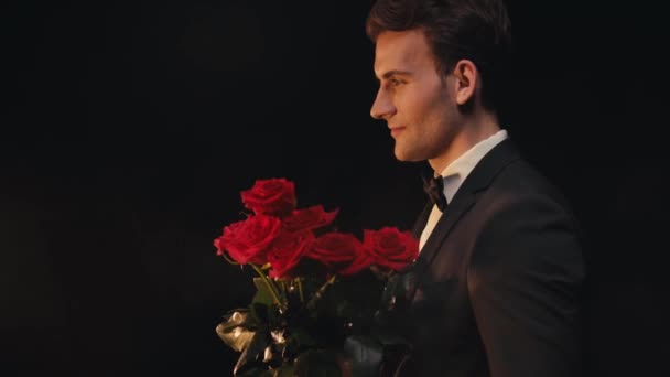Seitenansicht eines lächelnden jungen Mannes mit roten Rosen auf schwarzem Hintergrund  - Filmmaterial, Video