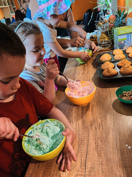 Group of children baking cupcakes, preparing ingredients, toppings, sprinkles for decorating cookies. Kids learning to cook, working together in kitchen at home. Concept of happy family - Foto, immagini