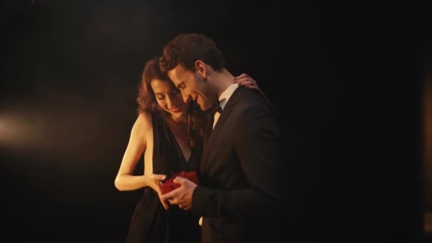 Szczęśliwa młoda kobieta przytula mężczyznę podczas otrzymywania pudełka na czarnym tle - Materiał filmowy, wideo