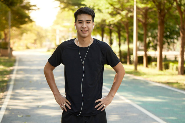 Молодой красивый азиат занимается спортом на открытом воздухе, слушая музыку в парке. - Фото, изображение