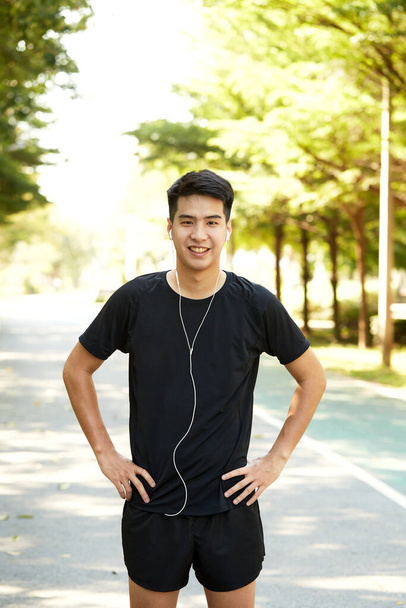 Giovane bell'uomo asiatico che si esercita all'aperto ascoltando musica nel parco. - Foto, immagini