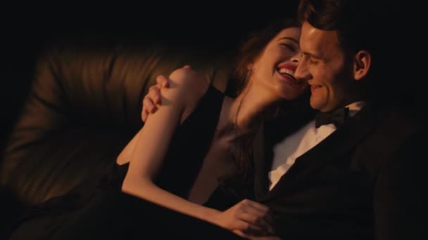 Allegro coppia elegante abbracciare e ridere sul divano isolato su nero  - Filmati, video