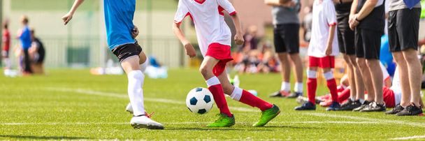 Παιδιά σε μονομαχία ποδοσφαίρου. Αγόρια σε δύο ποδοσφαιρικές ομάδες τρέχουν πίσω από την κλασική μπάλα ποδοσφαίρου στο σχολικό τουρνουά. Οριζόντια σπορ φόντο. Πόδια των νέων παικτών στο γήπεδο ποδοσφαίρου - Φωτογραφία, εικόνα