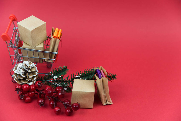 Happy New Year and Merry Christmas concept. Shopping cart with purchases and Christmas tree  - packages and boxes on red  background with copy space isolated. Online shopping and holiday sale concept. - Fotoğraf, Görsel