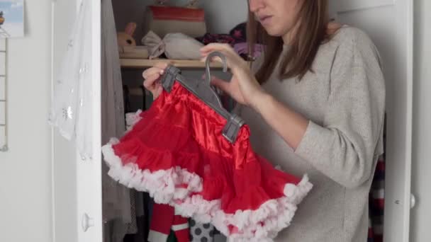 お母さんはハンガーの上のクローゼットの中に小さな娘のものを掛け、新年とクリスマスのための陽気な衣装を拾う - 映像、動画