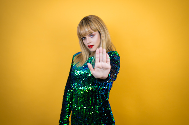 Beautiful blonde woman wearing a fancy dress over yellow background serious and doing stop sing with palm of the hand. - Photo, Image