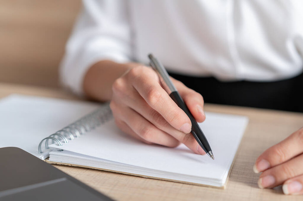 Female hand holding a pen making notes in notebook, closeup of blank paper list, woman office manager writing. Woman writing in office notebook, no face. Concept of writing - Foto, afbeelding