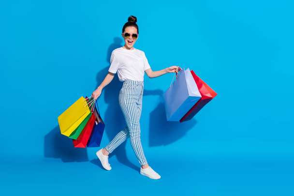 Full body profile side photo of positive cheerful girl shopping center client have leisure time go walk hold many off-sales bags wear white clothes isolated bright shine color background - Zdjęcie, obraz