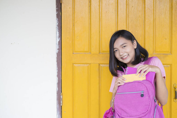 Portret student jong meisje op gele deur achtergrond met roze rugzak, glimlachende boeken dragen roze shirt en Jean. - Foto, afbeelding