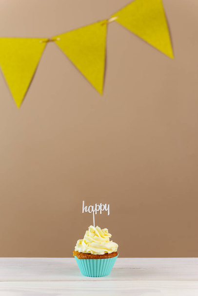 Cupcake mit "Happy" Topper auf braunem Hintergrund. - Foto, Bild