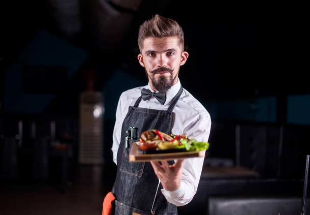 Friendly σερβιτόρος κρατά helpfully μαγειρεμένο πιάτο στο εστιατόριο. - Φωτογραφία, εικόνα