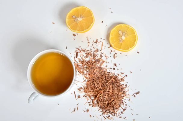 Ένα φλιτζάνι τσάι, φλοιό Catuaba και λεμόνι σε λευκό φόντο. Φυσικό τσάι από βότανα του φλοιού δέντρο Catuaba, φυσικό αφροδισιακό από τη Μπραζίλια - Φωτογραφία, εικόνα