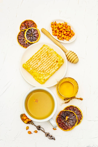 Curación de té de espino cerval de mar delicioso aromático lleno de vitaminas y microelementos. Miel, bayas frescas, panal y limón. Fondo masilla blanca, vista superior - Foto, imagen