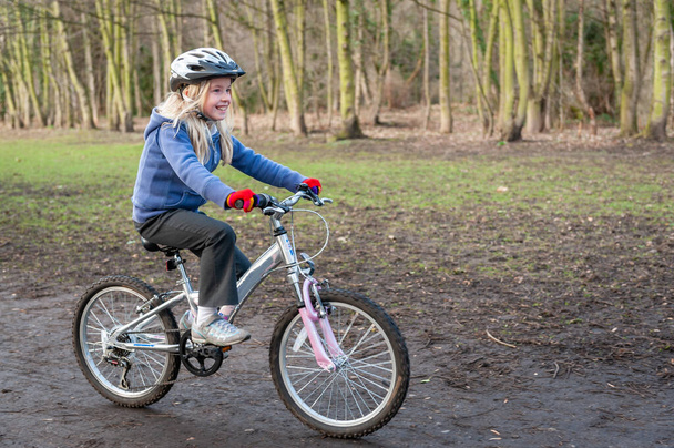 Uma menina feliz monta uma bicicleta ao longo de uma pista de campo - Foto, Imagem