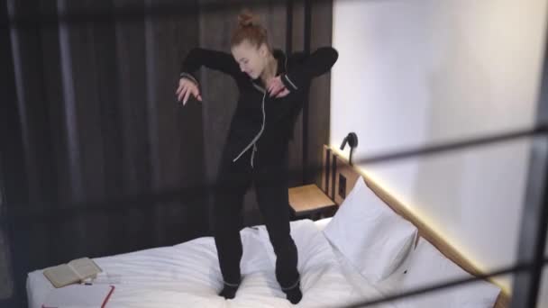 Joyful dance of carefree Caucasian teenage girl on bed. Wide shot of cheerful beautiful slim teenager dancing in bedroom. Relaxed teen having fun at home. Lifestyle and adolescence concept. - Metraje, vídeo