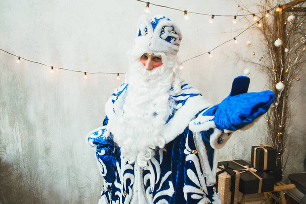 Санта Клаус в синьому хутрі стоїть на задньому плані садівника Нового Року і показує рукою в рукавичці до камери. - Фото, зображення