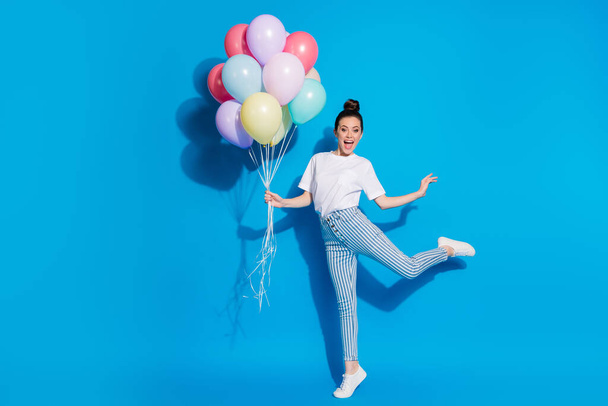 Full length body size view of nice attractive funky comic childish playful cheerful girl jumping holding in hand bunch air balls having fun isolated on bright vivid sine vibrant blue color background - 写真・画像
