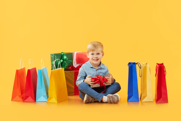 Sale of childrens products. Portrait of fun little child boy  on yellow background holding shopping bags, package. Looking at the camera. Banner. Space for text.  - Foto, imagen